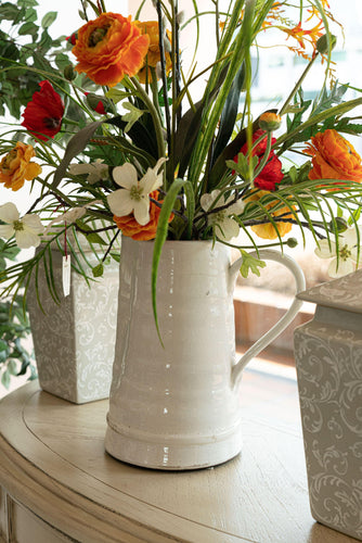 An Artificial flower arrangement on a white-colored vase with handle